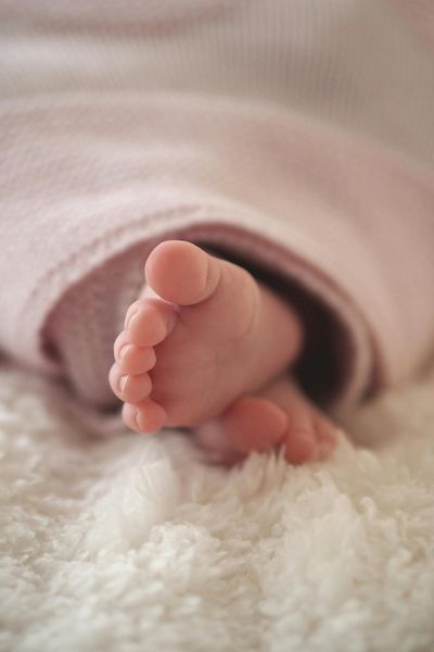 Baby's feet and toes peeking out the end of a pink blanket with a cream, fluffy blanket underneath.