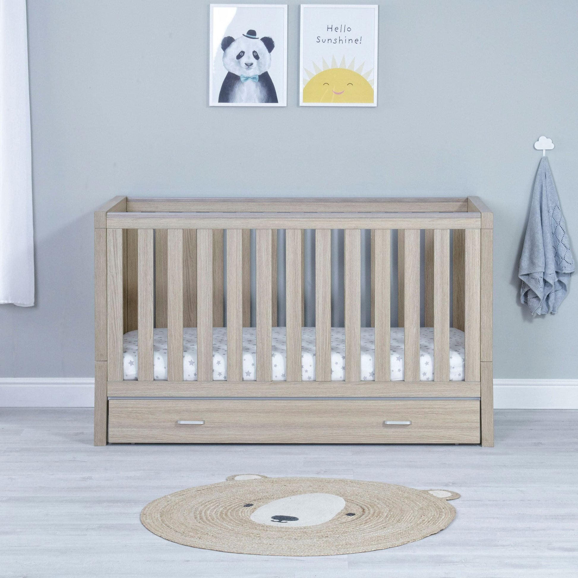 Babymore-Luno-Cot-Bed-with-drawer-oak-in-nursery-setting-as-cot-front